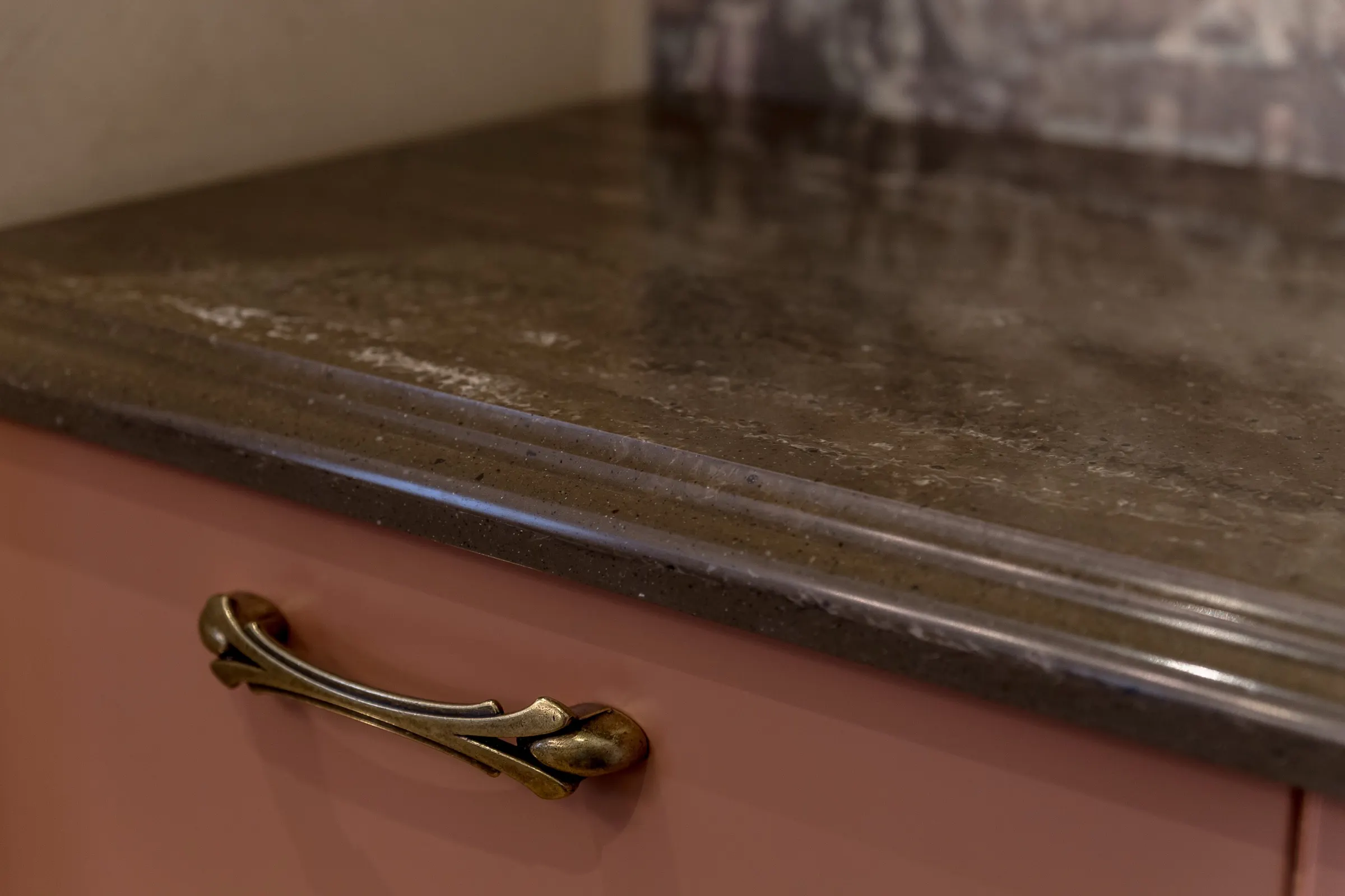 Narożnik blatu z fakturą kamienną, w tle fragment fartucha z tego samego materiału